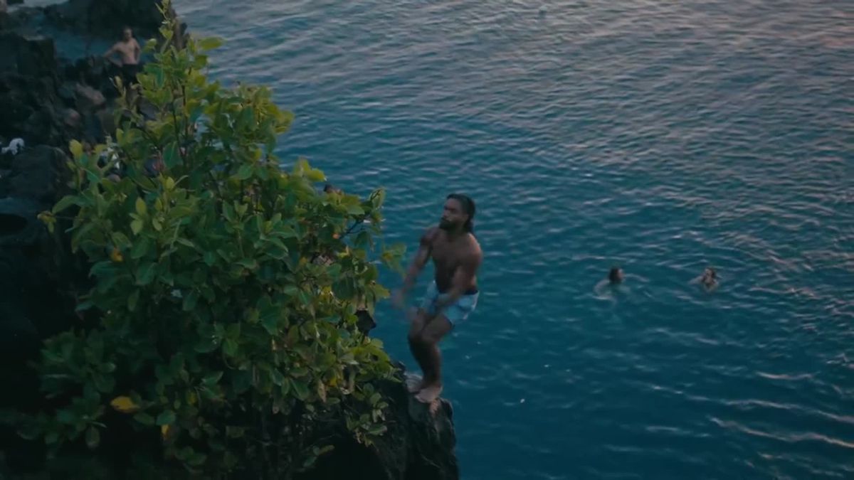 Un homme s'apprête à sauter d'une falaise dans la mer, des baigneurs en contrebas