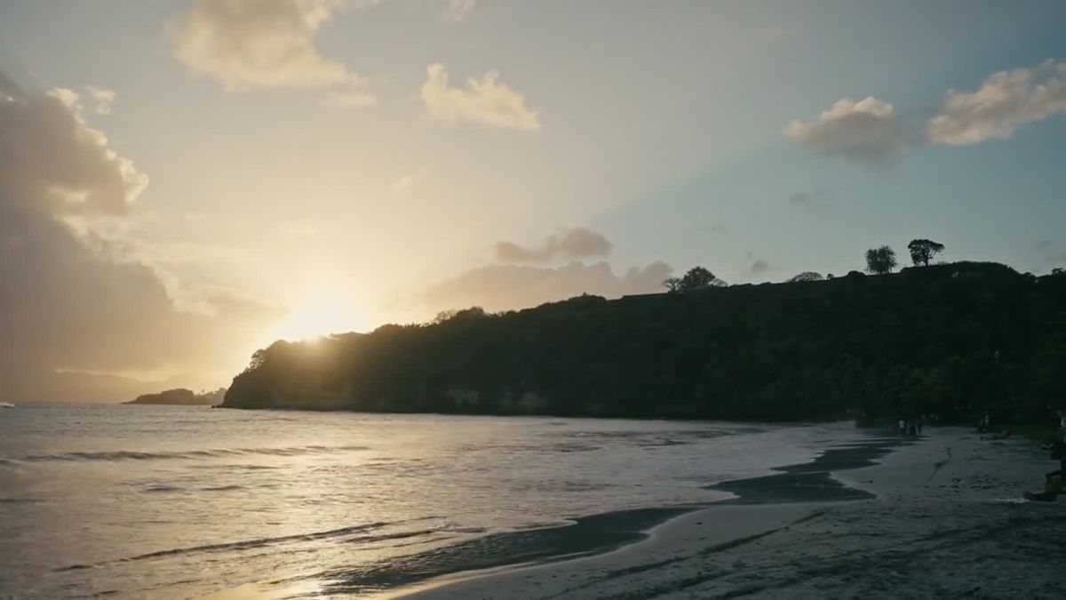 Plage au coucher du soleil, vagues et morne boisé à contre-jour